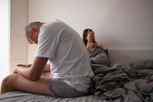 Homem sentando na cama com parceira refletindo sobre necessidade de tratamento para ejaculação precoce​.