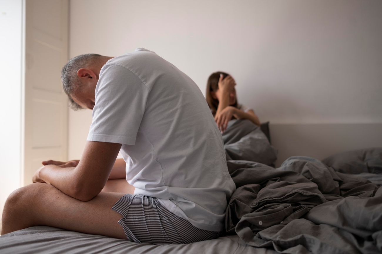 Homem sentando na cama com parceira refletindo sobre necessidade de tratamento para ejaculação precoce​.