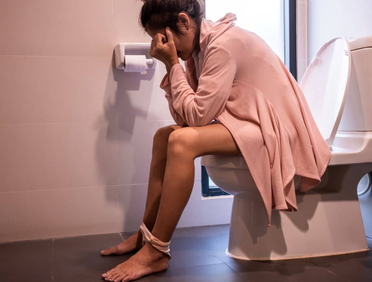 Mulher sentada no vaso sanitário com aparente desconforto que pode ser causado por fissura anal.
