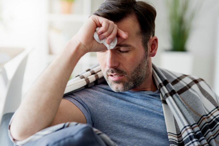 Homem com sintomas de polipose nasal que se assemelham a uma gripe sentado no sofá.