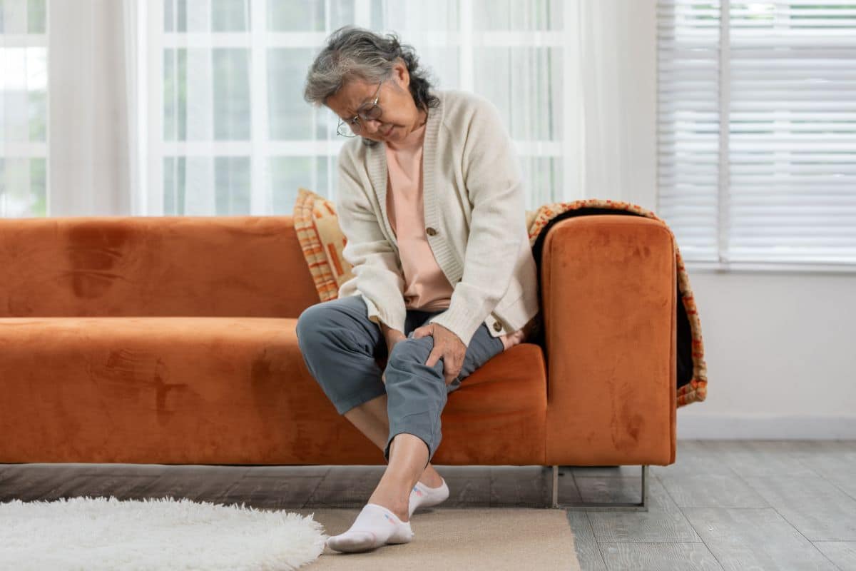 Idosa sentada com dor na perna, ilustrando sintomas comuns da doença arterial periférica em pessoas com diabetes.